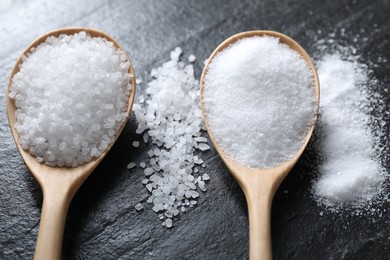 Photo of Organic salt in spoons on black table, closeup