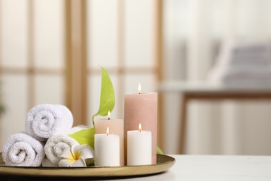 Spa composition. Burning candles, plumeria flower, green leaves and towels on white table indoors, space for text