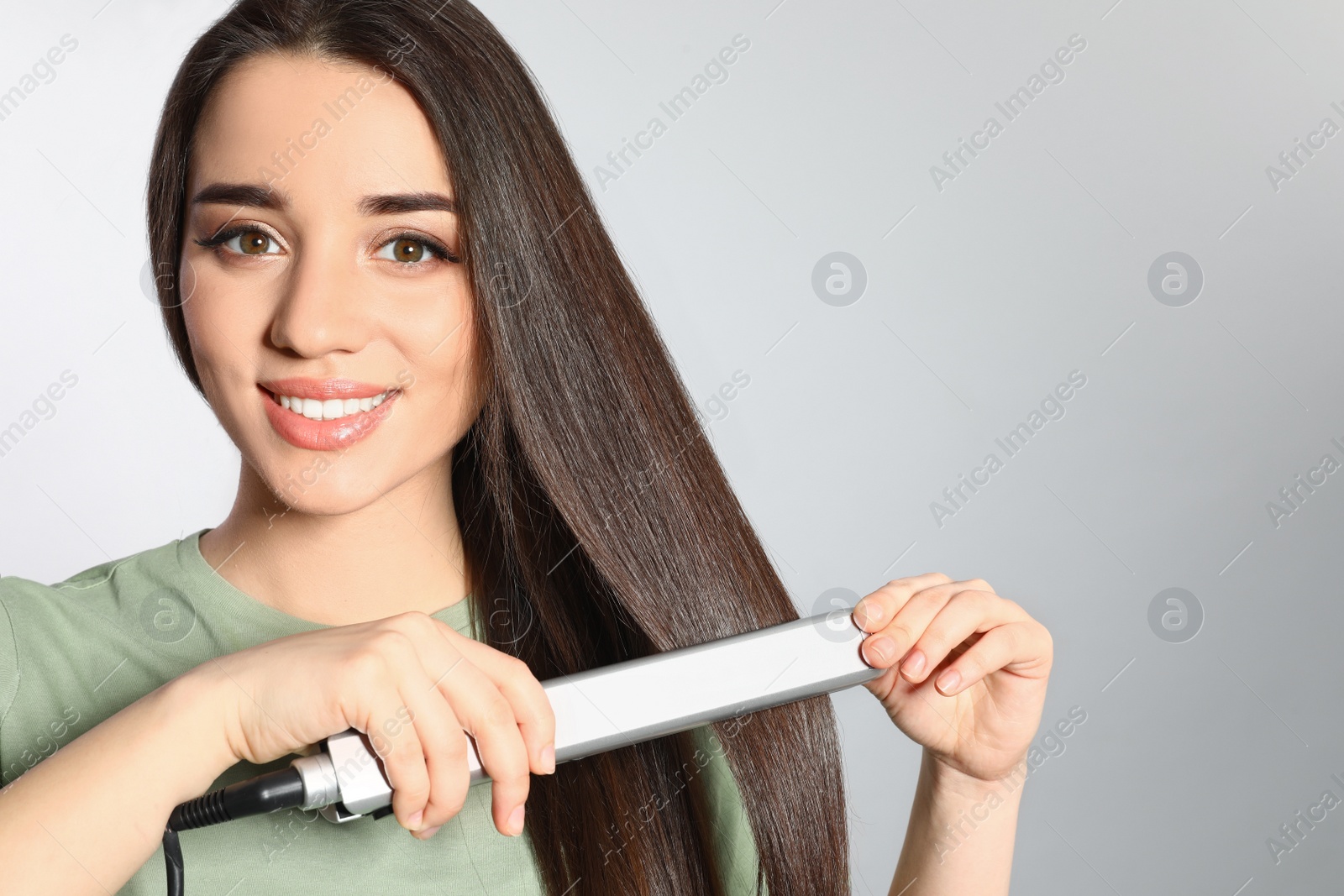 Photo of Happy woman using hair iron on grey background. Space for text