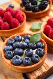 Photo of Tartlets with different fresh berries on wooden board, closeup. Delicious dessert