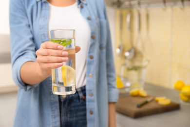Photo of Young woman with glass of lemon water in kitchen, closeup. Space for text