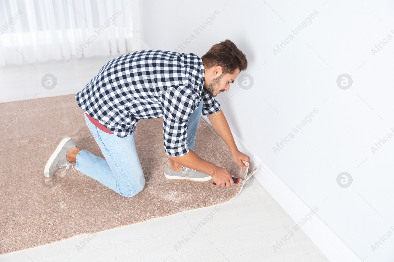 Photo of Man cutting new carpet flooring indoors. Space for text