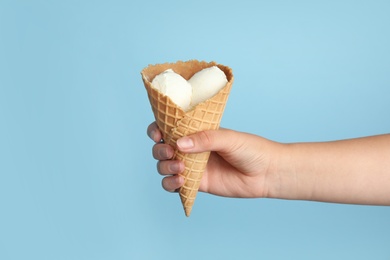 Woman holding delicious ice cream in wafer cone on blue background, closeup