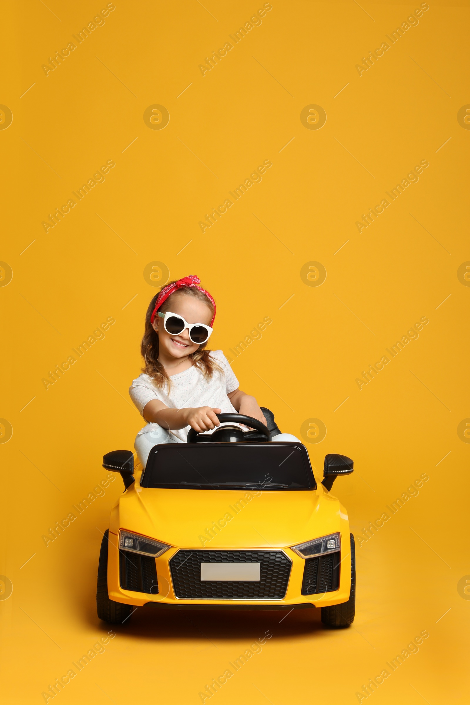 Photo of Cute little girl driving children's electric toy car on yellow background