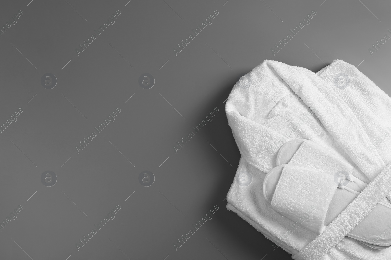 Photo of Clean folded bathrobe and slippers on grey background, top view. Space for text