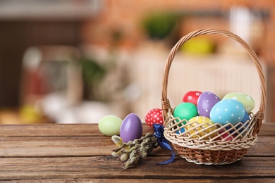 Image of Wicker basket with bright painted Easter eggs on wooden table indoors, space for text
