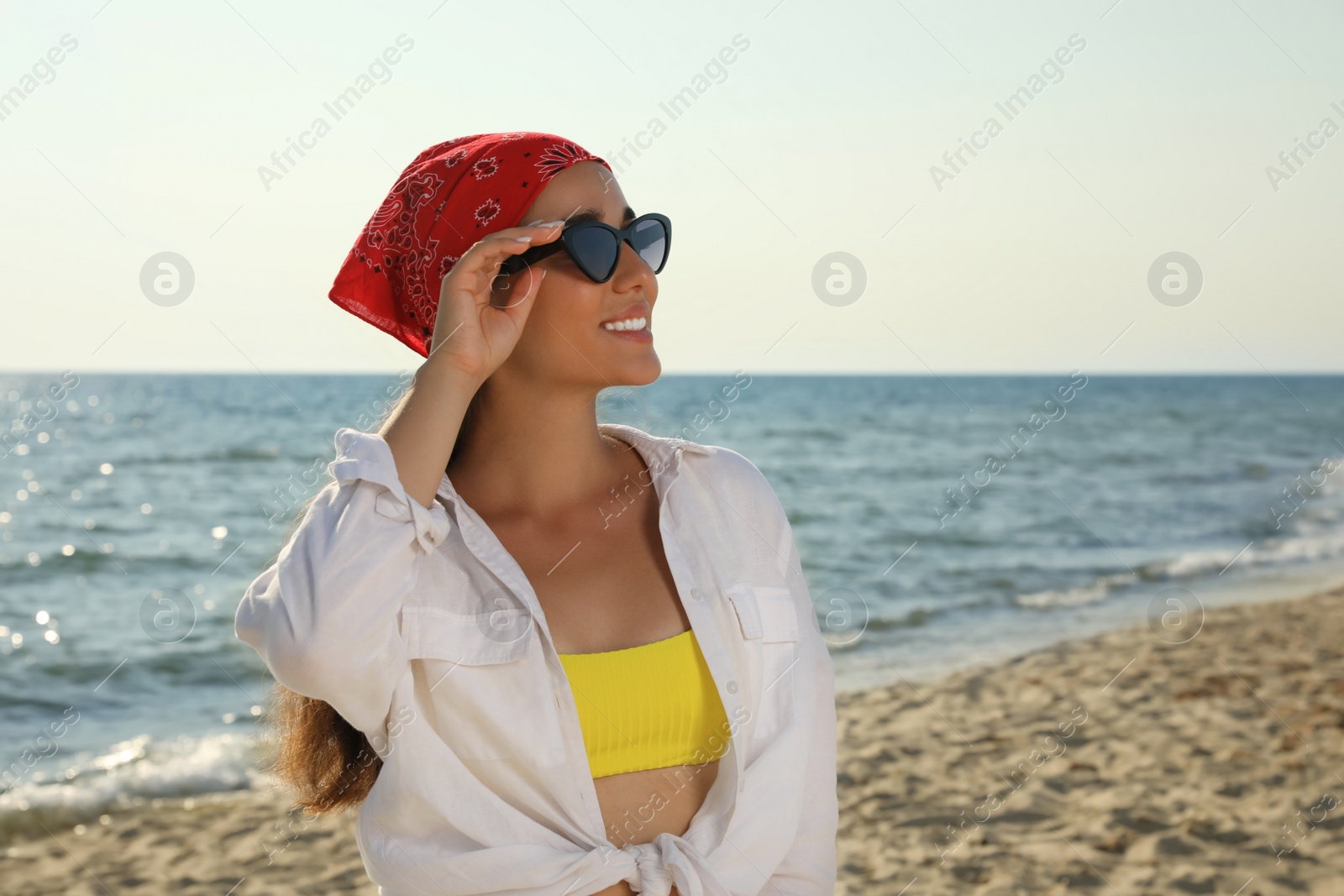 Photo of Young woman with sunglasses and bandana at beach. Sun protection care