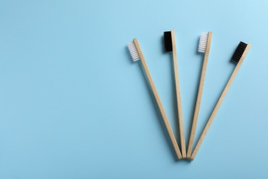 Photo of Bamboo toothbrushes on light blue background, flat lay. Space for text