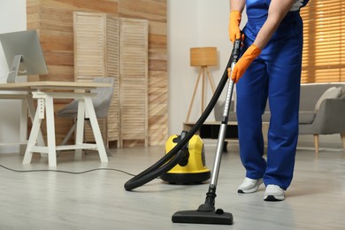 Janitor in uniform vacuuming floor indoors, closeup. Space for text