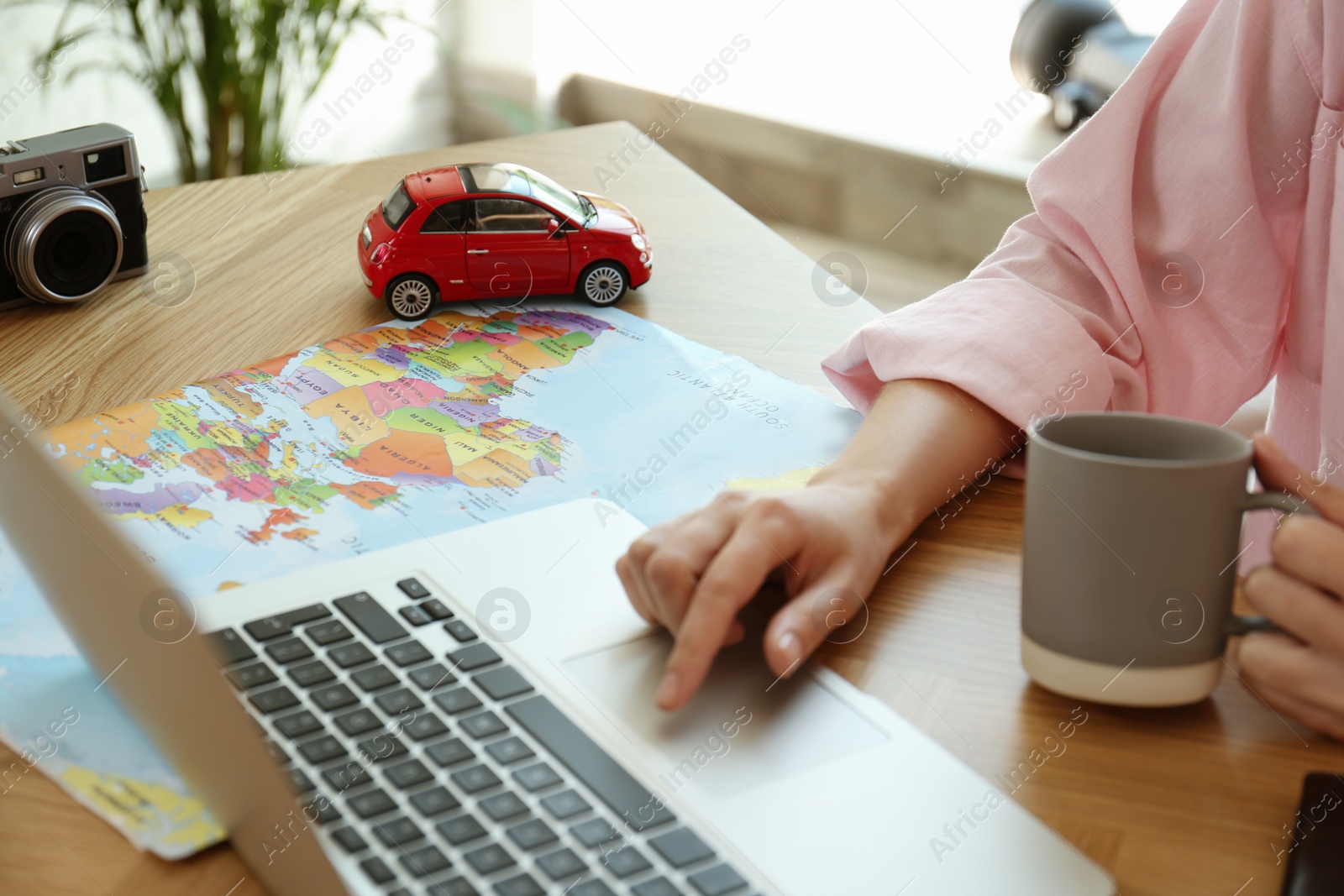 Photo of Woman using laptop to plan trip at wooden table, closeup