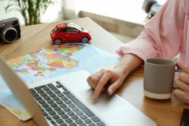 Photo of Woman using laptop to plan trip at wooden table, closeup