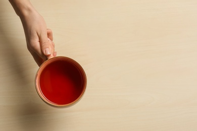 Woman holding cup of tea at wooden table, top view. Space for text