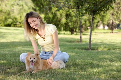 Photo of Young woman with her cute dog on green grass in park, space for text
