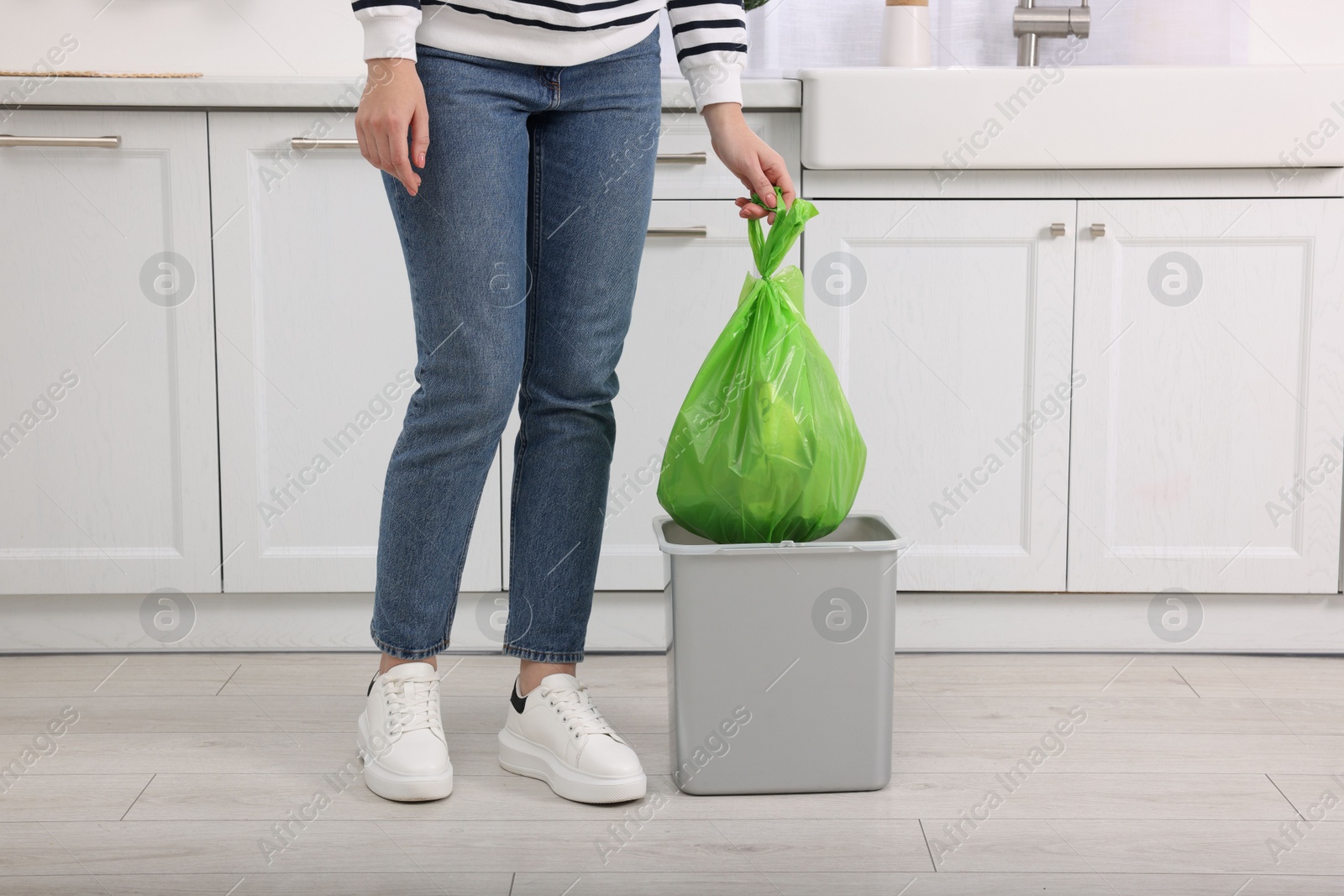 Photo of Woman taking garbage bag out of trash bin in kitchen, closeup