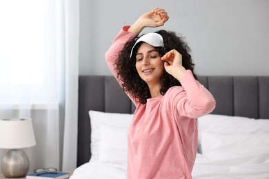 Photo of Beautiful young woman in stylish pyjama and sleep mask on bed at home