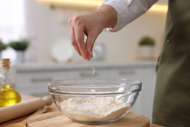 Photo of Making bread. Man putting salt into bowl with flour at wooden table in kitchen, closeup