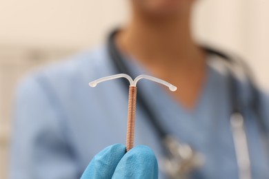 Doctor holding T-shaped intrauterine birth control device on blurred background, closeup