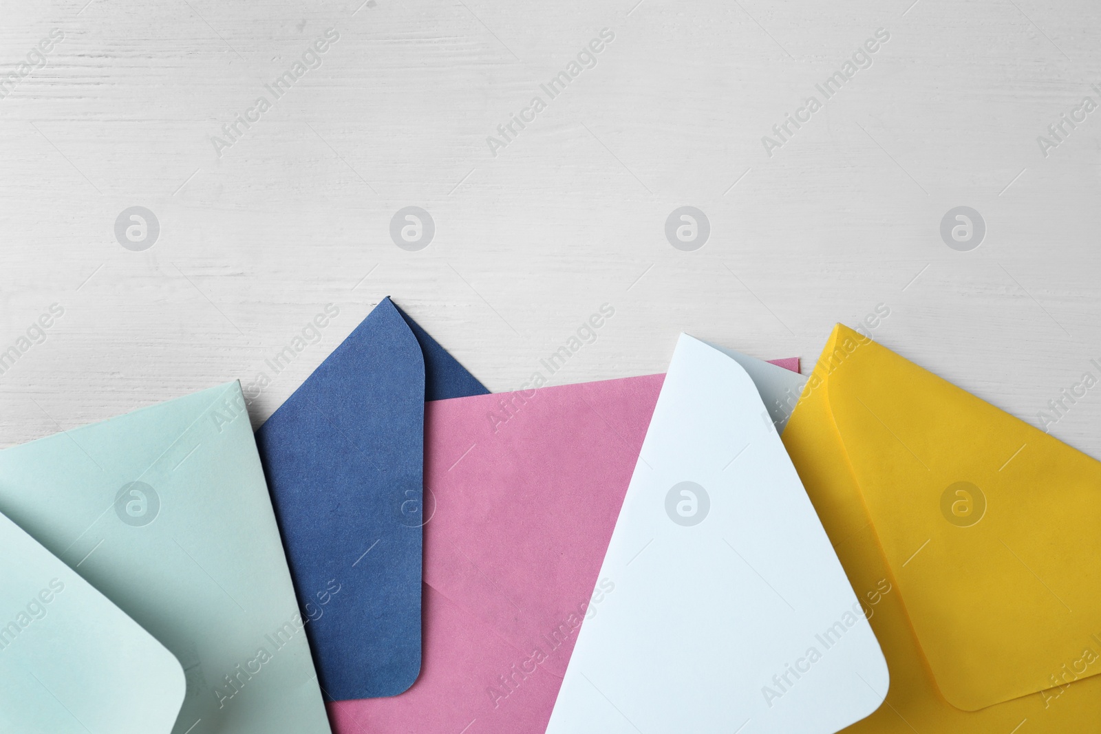 Photo of Colorful paper envelopes on white wooden table, flat lay. Space for text