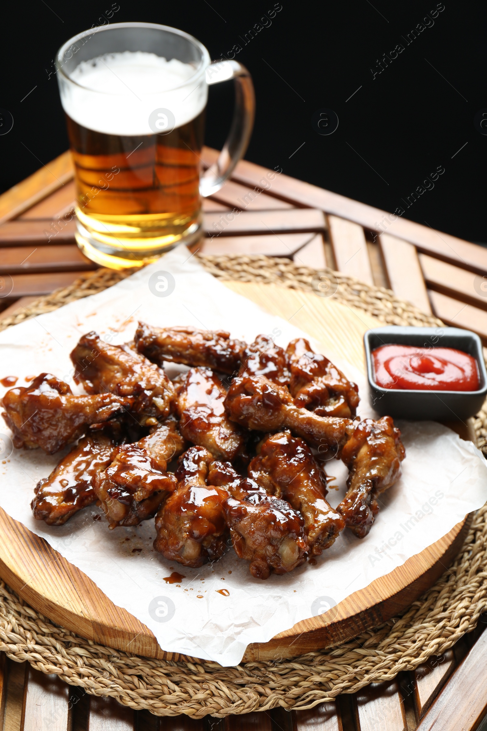 Photo of Tasty chicken wings, mug of beer and ketchup on wooden table. Delicious snack