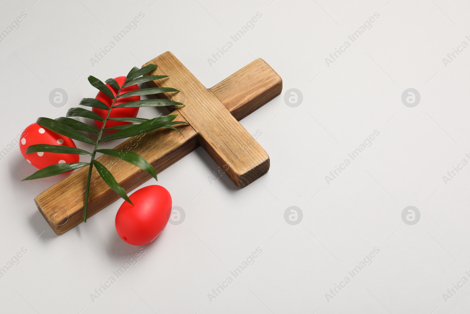 Photo of Wooden cross, painted Easter eggs and palm leaf on light grey background, space for text