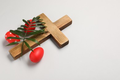 Photo of Wooden cross, painted Easter eggs and palm leaf on light grey background, space for text