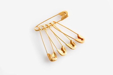 Golden safety pins on white background, flat lay