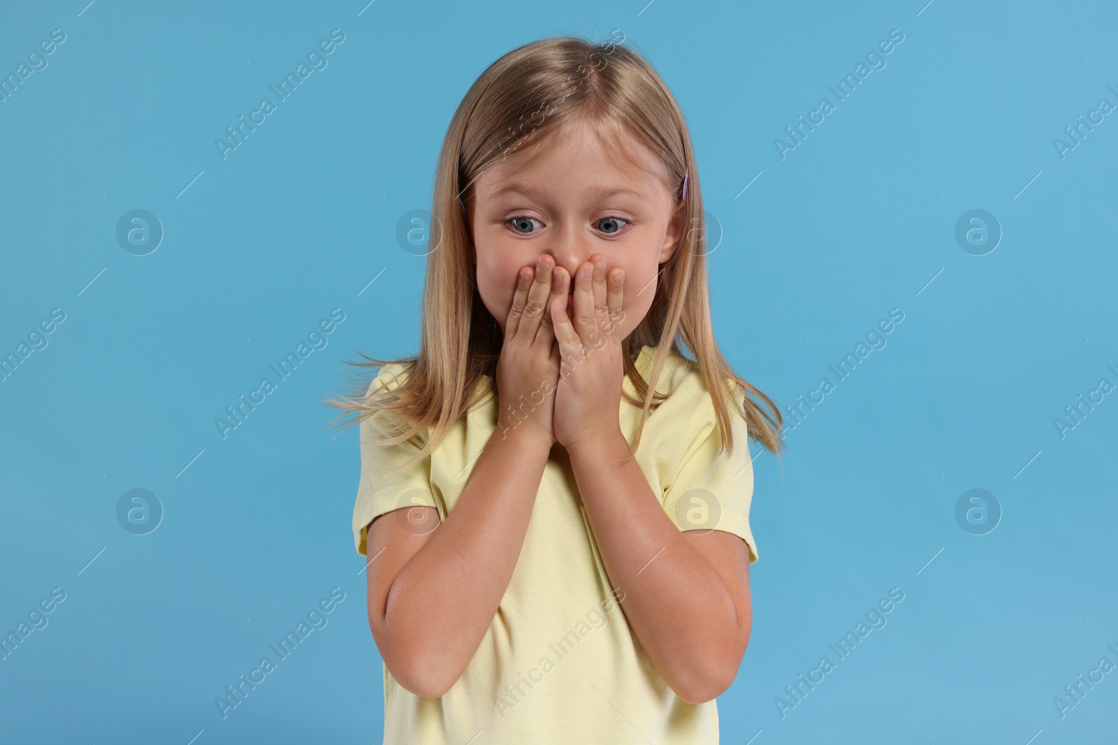 Photo of Embarrassed little girl covering mouth with hands on light blue background