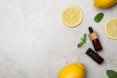 Photo of Bottles of citrus essential oil and fresh lemons on light table, flat lay. Space for text