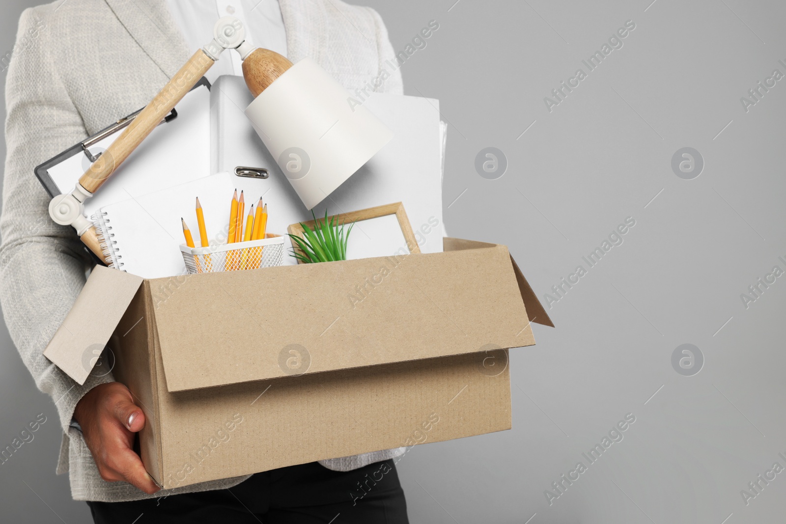 Photo of Unemployed man with box of personal office belongings on light grey background, closeup. Space for text