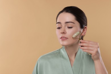 Young woman massaging her face with jade roller on beige background. Space for text