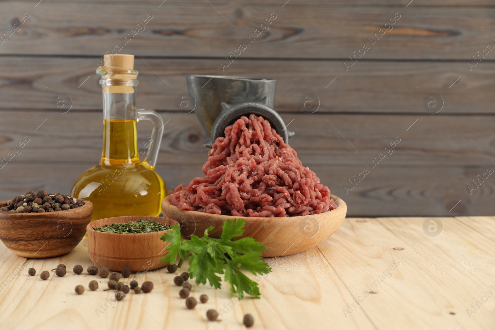 Photo of Mincing beef with manual meat grinder. Parsley, oil and spices on wooden table, space for text