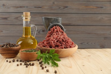 Photo of Mincing beef with manual meat grinder. Parsley, oil and spices on wooden table, space for text