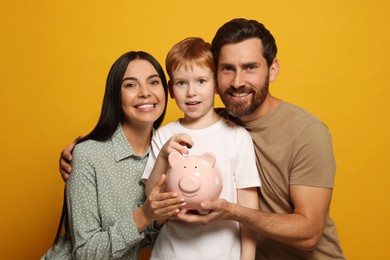 Photo of Happy family with ceramic piggy bank on orange background