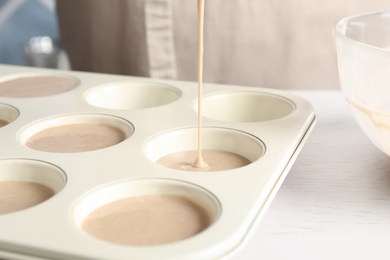 Pouring batter into cupcake tray at white table in kitchen, closeup