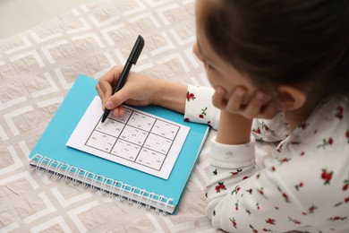 Photo of Little girl solving sudoku puzzle on bed
