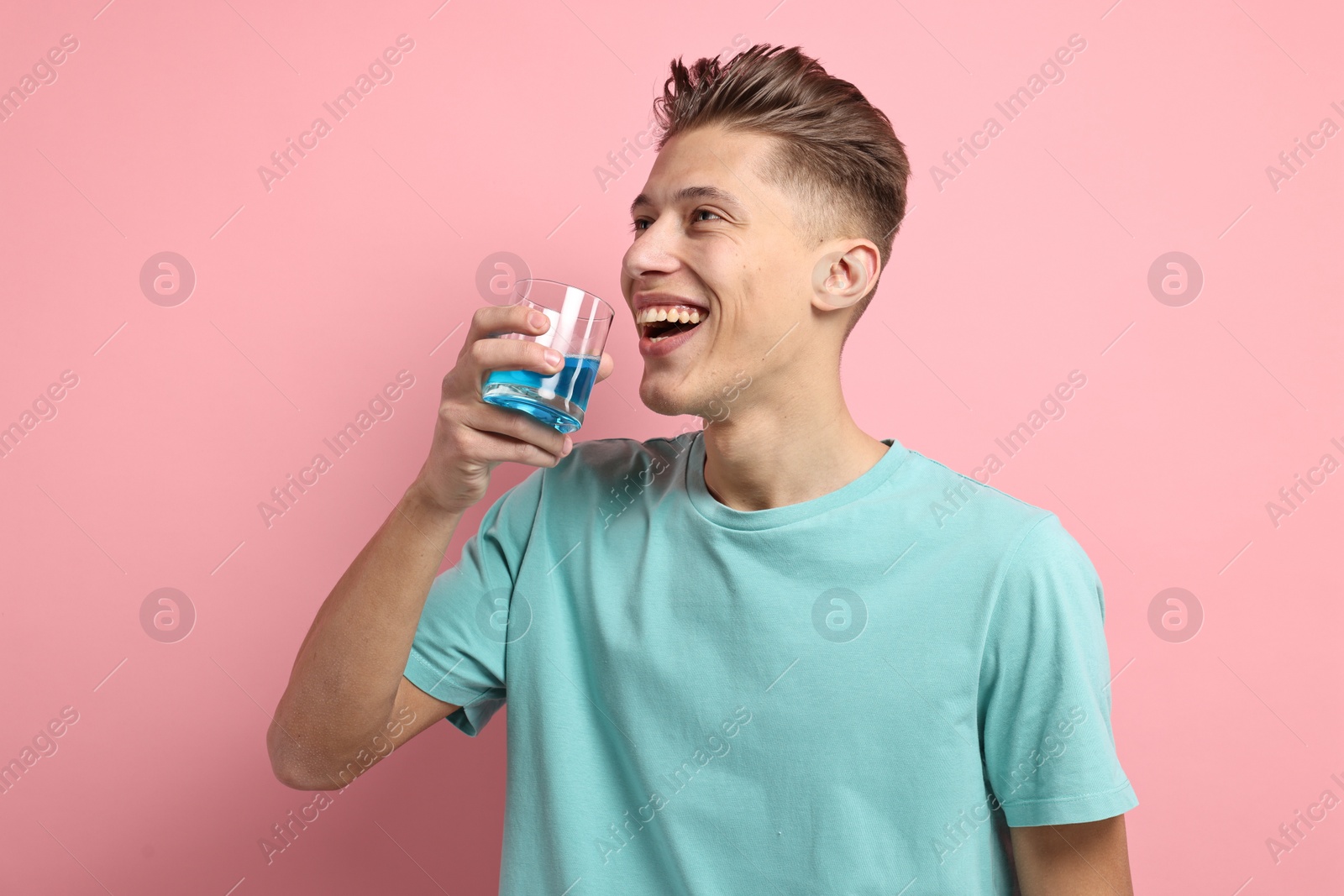 Photo of Young man using mouthwash on pink background