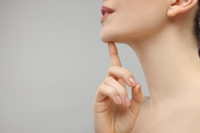 Woman touching her chin on grey background, closeup. Space for text