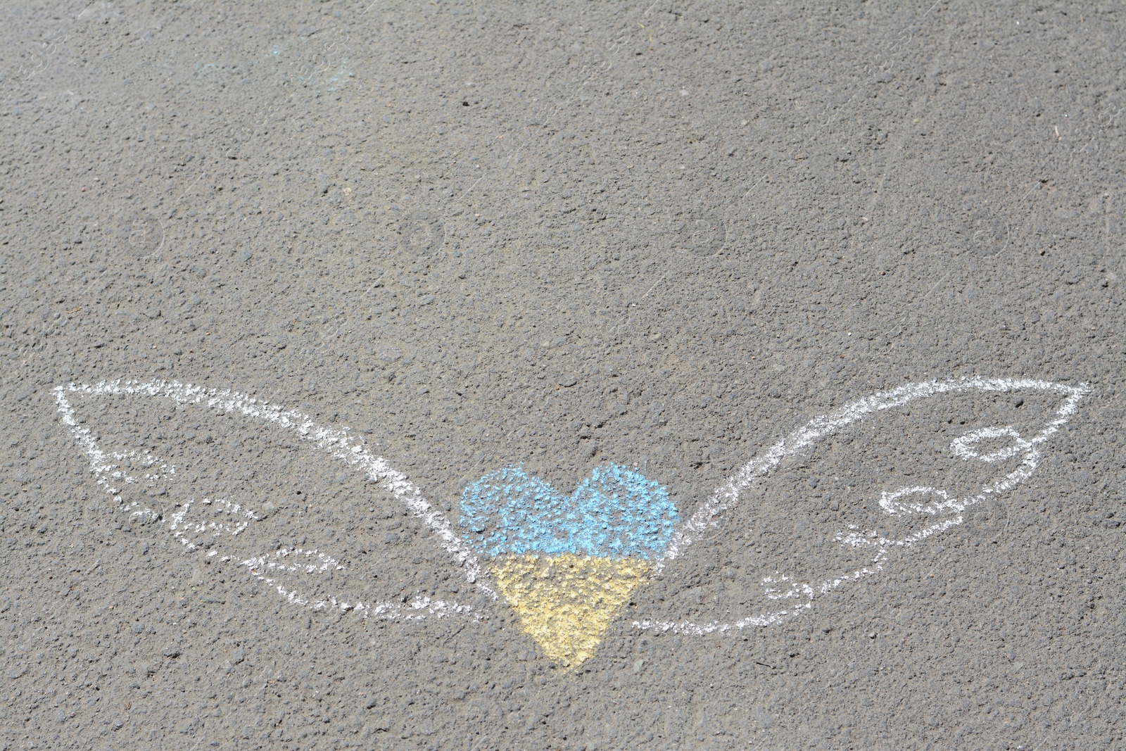 Photo of Heart and wings drawn with blue and yellow chalks on asphalt outdoors, top view. Space for text