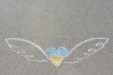 Heart and wings drawn with blue and yellow chalks on asphalt outdoors, top view. Space for text