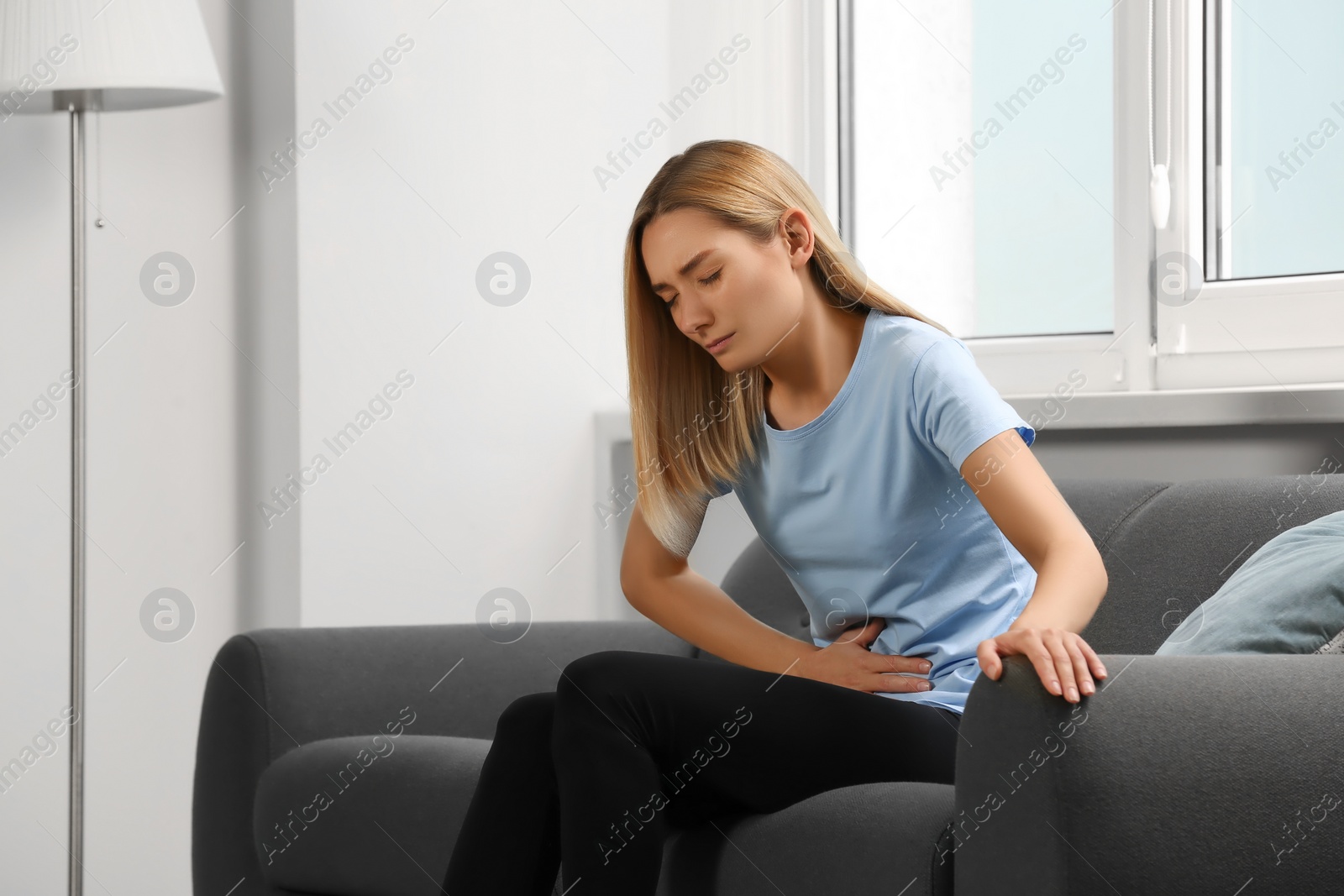 Photo of Young woman suffering from menstrual pain on sofa at home