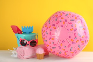 Photo of Pink inflatable ball, blanket, sunglasses and sand beach toys on white wooden table against yellow background