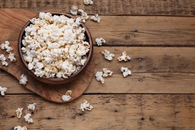 Photo of Bowl of tasty popcorn on wooden table, above view. Space for text