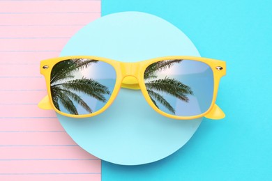 Image of Stylish sunglasses on color background, top view. Sky and palm tree leaves reflecting in lenses