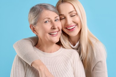 Family portrait of young woman and her mother on light blue background