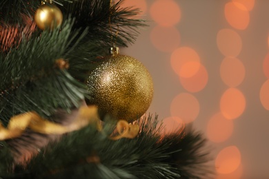 Photo of Golden holiday baubles hanging on Christmas tree against blurred festive lights, closeup. Space for text