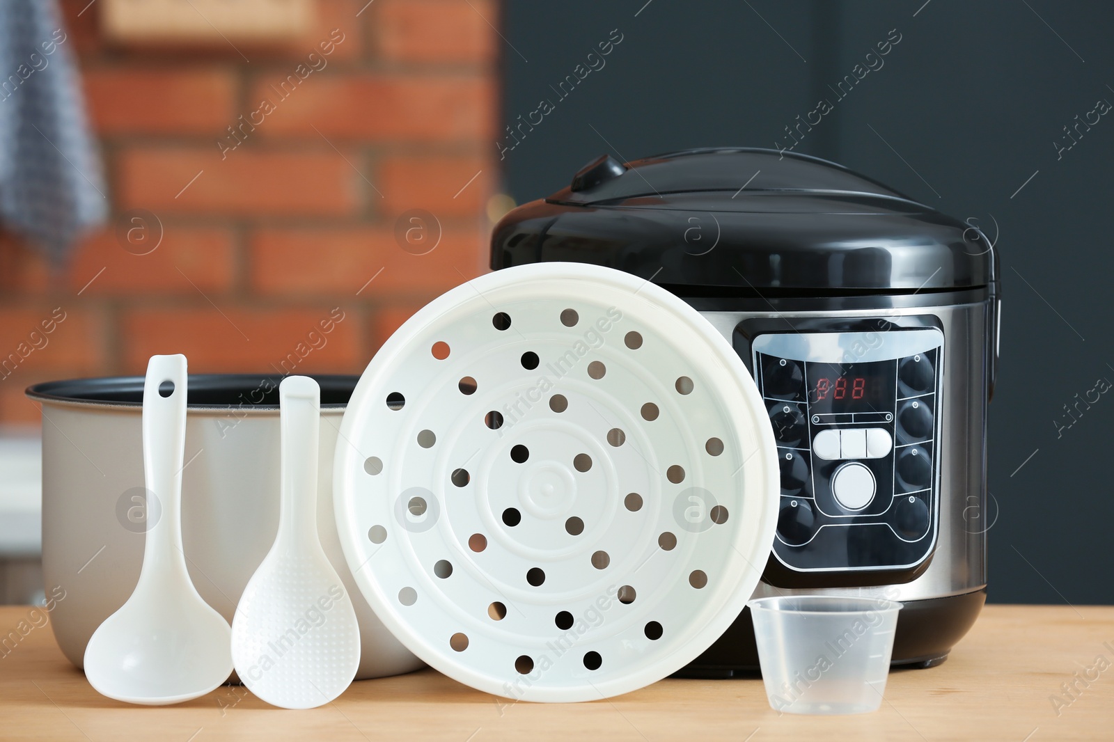 Photo of Modern electric multi cooker, parts and accessories on table in kitchen