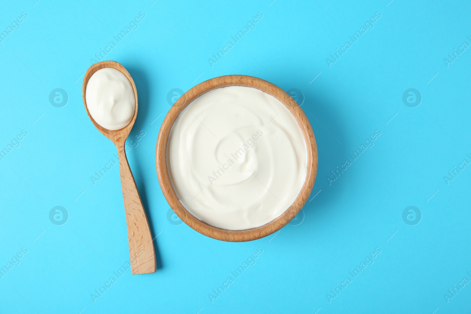 Photo of Wooden bowl and spoon of sour cream on light blue background, flat lay