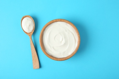 Photo of Wooden bowl and spoon of sour cream on light blue background, flat lay