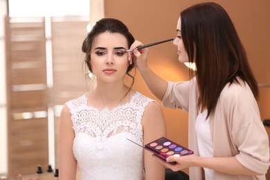 Photo of Professional makeup artist working with young bride in salon