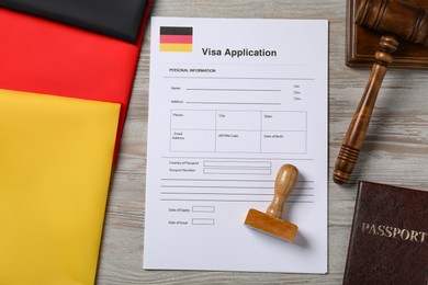 Photo of Immigration to Germany. Visa application form, passport, gavel and stamp on wooden table, flat lay